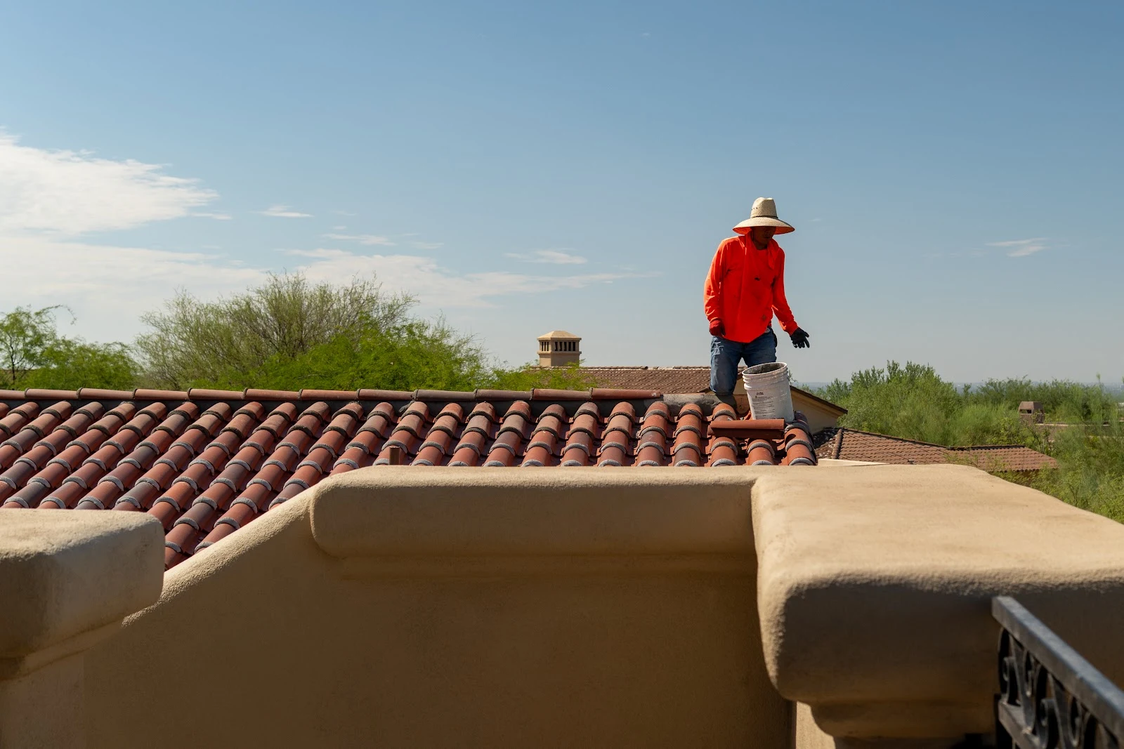 Crew member on a clay tile roof behind a stucco parapet